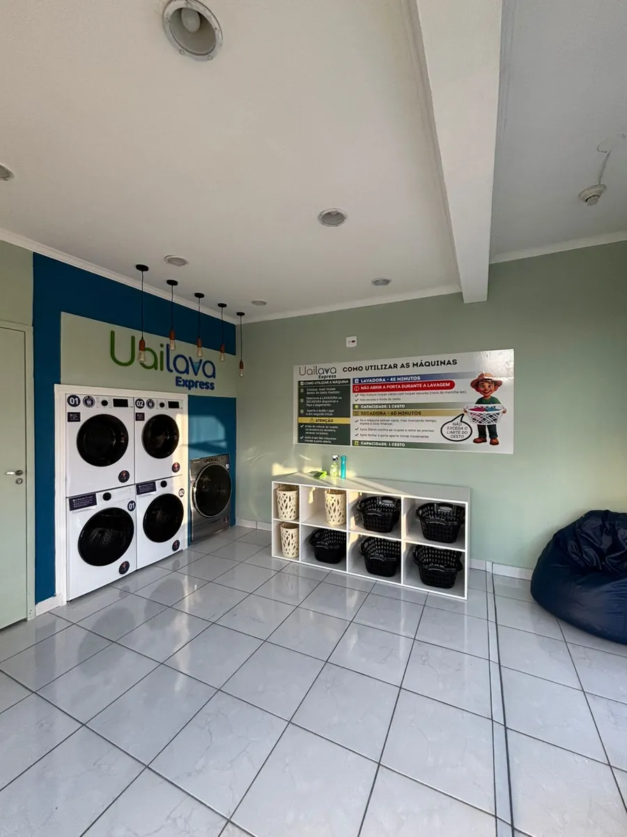 O salão inteiro da loja: piso claro, pé-direito alto, o mural "Como utilizar as máquinas" ao lado dos cestos e um puff azul no canto.